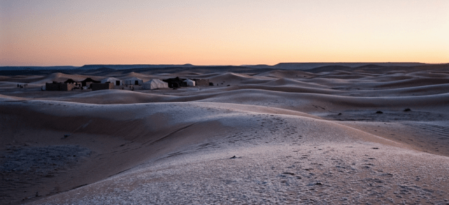 Desert camp with tents surrounded by sand dunes at twilight
